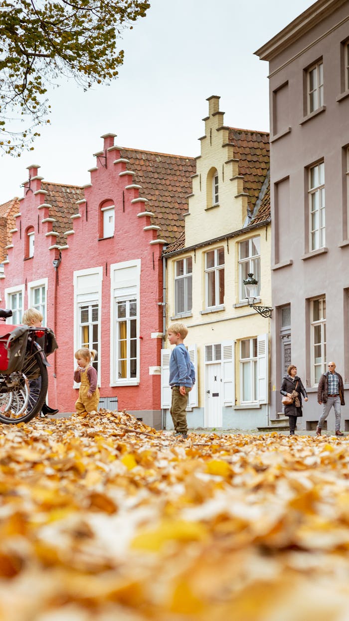 Colorful houses line a leaf-strewn street as children play joyfully in autumn.