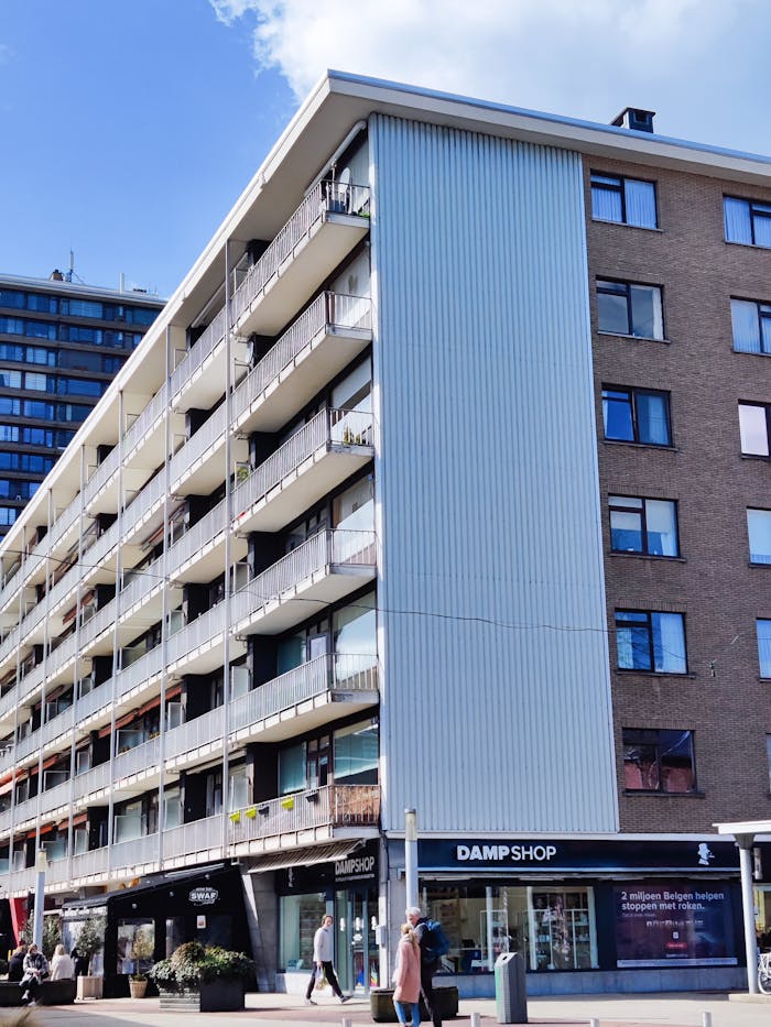 Modern urban apartment building with shops on street level, captured on a sunny day.